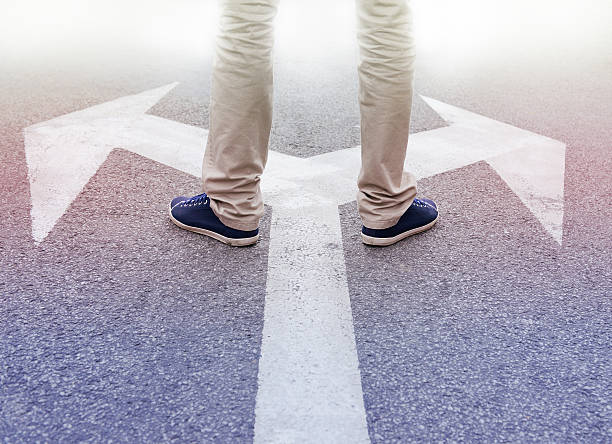 arrows painted on asphalt. young man standing hesitating to make a decision. arrows painted on asphalt. young man standing hesitating to make a decision.